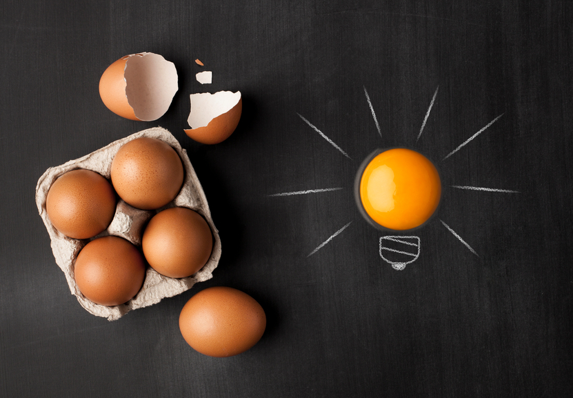 Egg yolk ball forming a shape of illuminated light bulb on blackboard