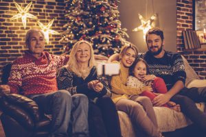 Extended family sitting on sofa with christmas tree in background. They are taking selfie with selfie stick. Evening or night with beautiful yellow lights lightning the scenes.